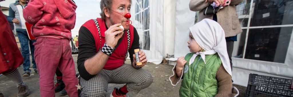 Clown blåser såpbubblor, ett litet barn tittar nyfiket på