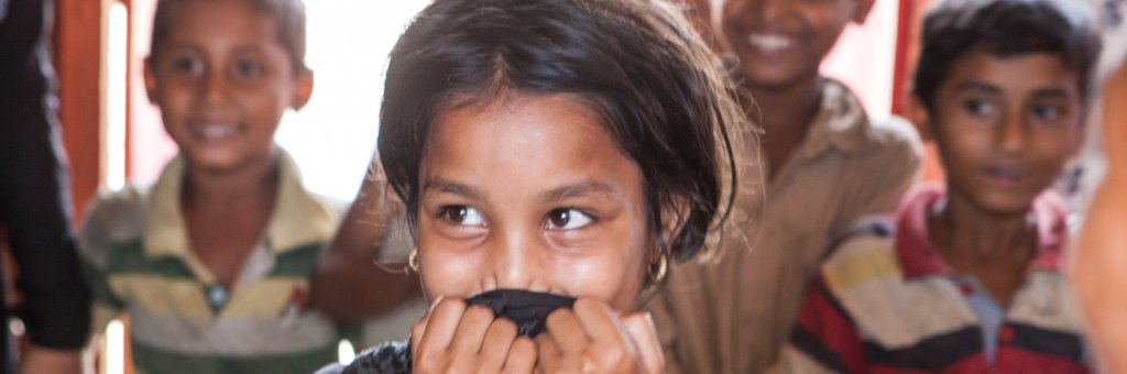 Närbild på flicka som ler och döljer munnen med sina händer