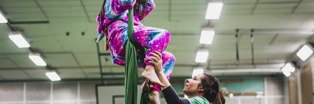 Ett barn hänger i tyg i taket och en pedagog står nedanför och håller i barnets fötter