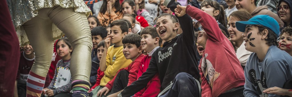 Skrattande barn i ett publikhav framför clowner på scen