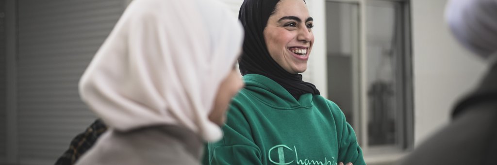 En tjej i hijab och grön tröja står och skrattar