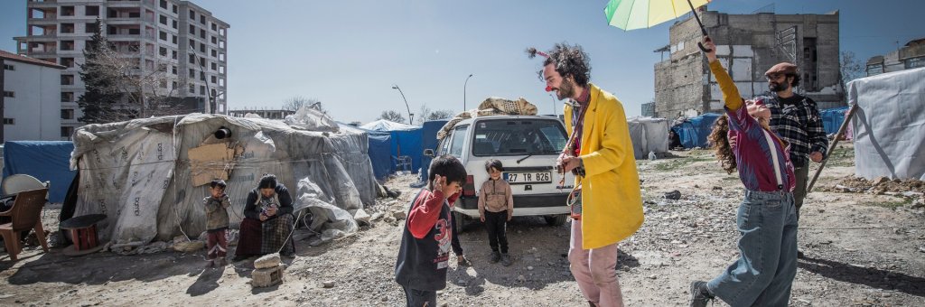 En artist med ett färgglatt paraply, en artist som spelar musik, ett barn som dansar