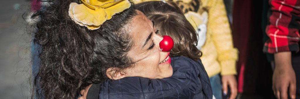 En clown i röd näsa blir omkramad av ett barn