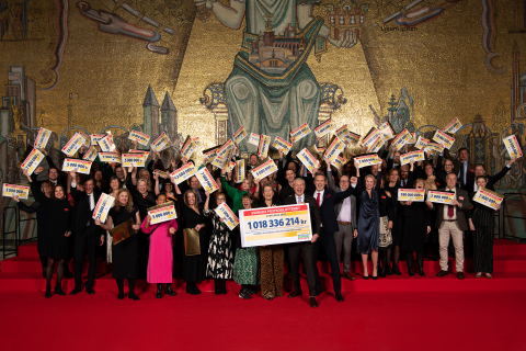 Foto från Postkodlotteriets årliga gala där förmånstagarna får sina checkar. En stor grupp människor från de olika organisationerna står på bilden och håller upp sina checkar och ler.