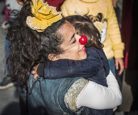 Ett litet barn kramar om en clown med röd näsa som ler
