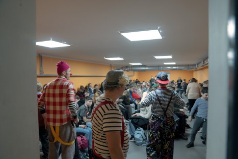 Tre artister i mönstrade kläder framför en publik i ett litet rum