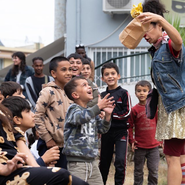 Flera barn står runt en artist och tittar på ett magitrick, de ler
