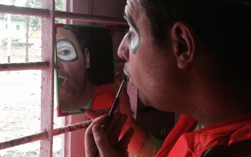 Clown sminkar sig och speglar sig i en handspegel