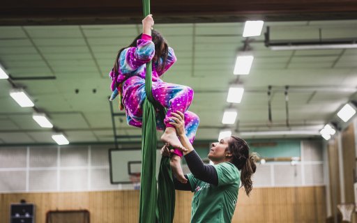 Ett barn hänger i tyg i taket och en pedagog står nedanför och håller i barnets fötter